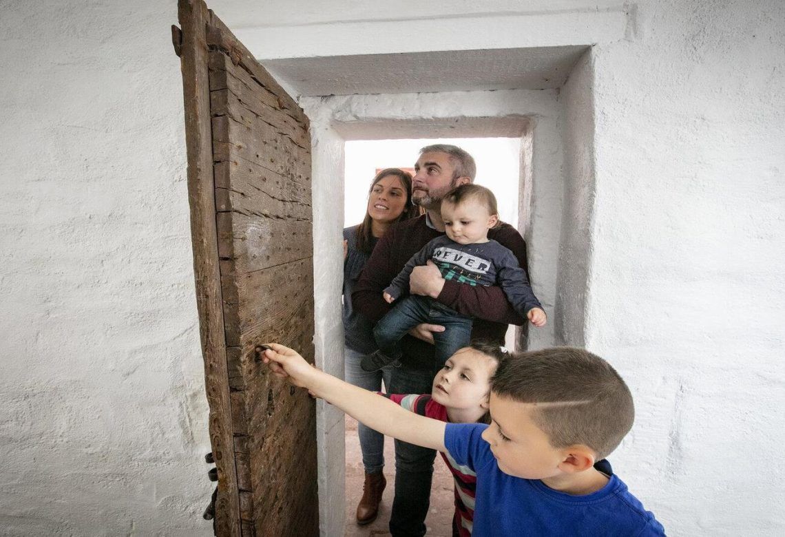 A family with three young children peering through an old wooden door at Down County Museum.